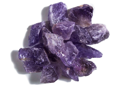 Violet raw, natural crystal amethyst pieces clustered together on a white background.