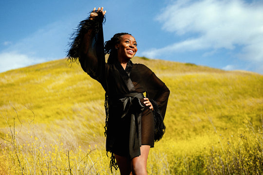 Black female model posing on a grassy hill wearing EDEN feather trim robe by SHOLAYIDÉ.