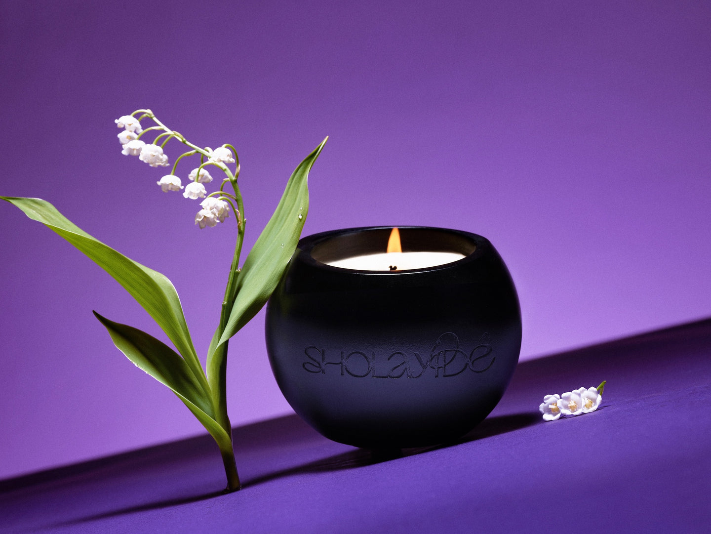 FAVORED vegan scented candle by SHOLAYIDÉ paired with a cluster of Lily of the Valley flowers