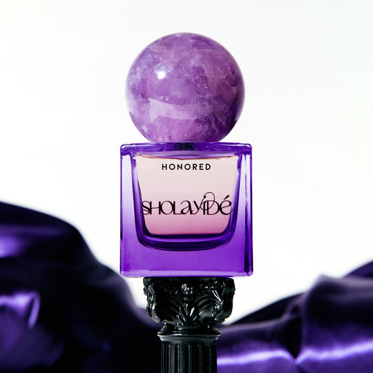 SHOLAYIDE Honored Eau de Parfum on black pedestal with purple satin background
