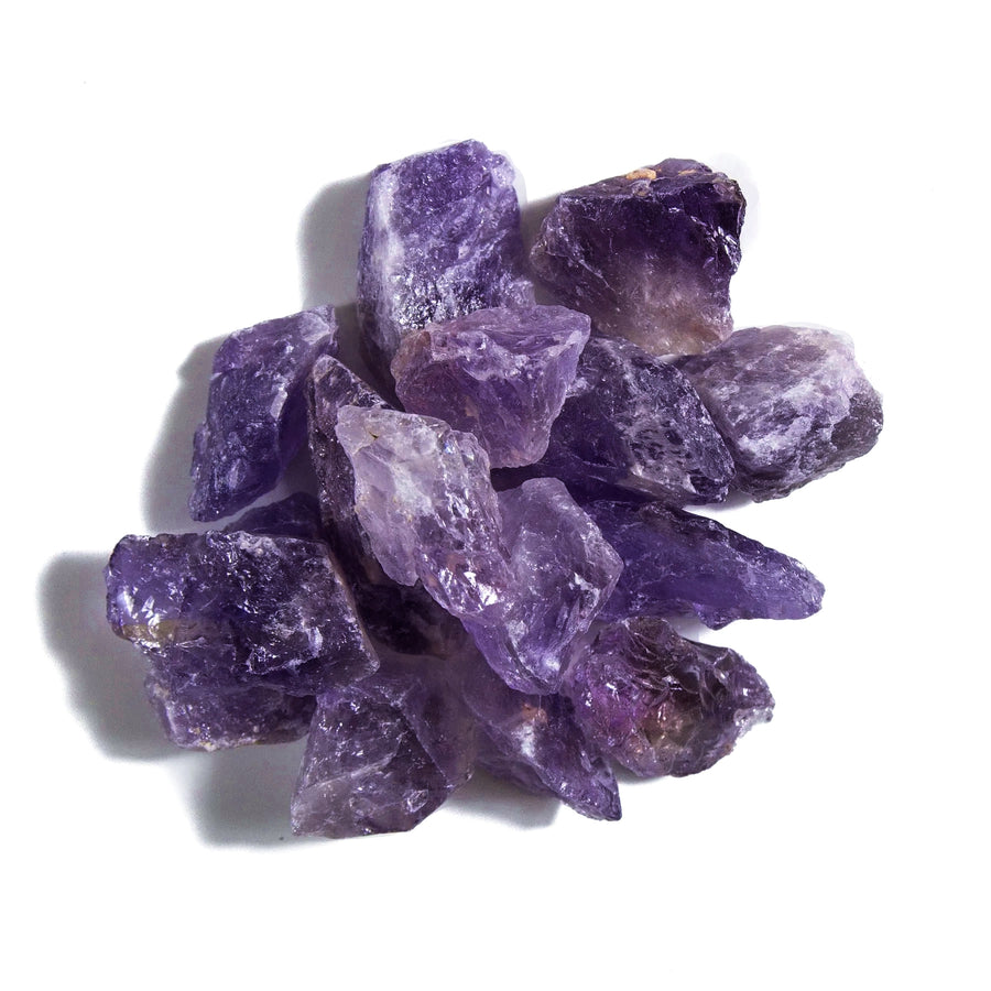 Violet purple colored raw amethyst crystal stones piled together on a white background.