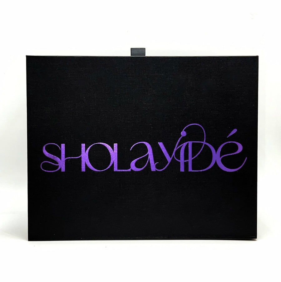 Black textured candle box packaging with SHOLAYIDÉ logo foil printed in purple on white background.