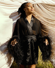 Black female model posing on a grassy hill wearing the EDEN feather trim robe by SHOLAYIDÉ