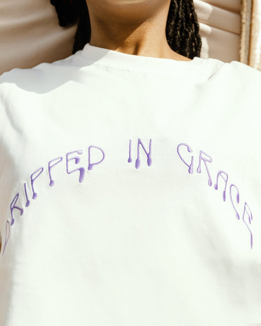Close up shot of GRACE white t-shirt details with purple Dripped in Grace embroidery detail by SHOLAYIDÉ.