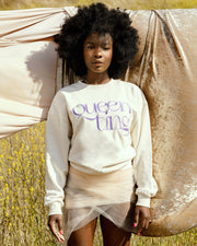 Beautiful black female model with afro hair on a grass hill wearing the cream Queen Ting embroidery sweatshirt by SHOLAYIDÉ.