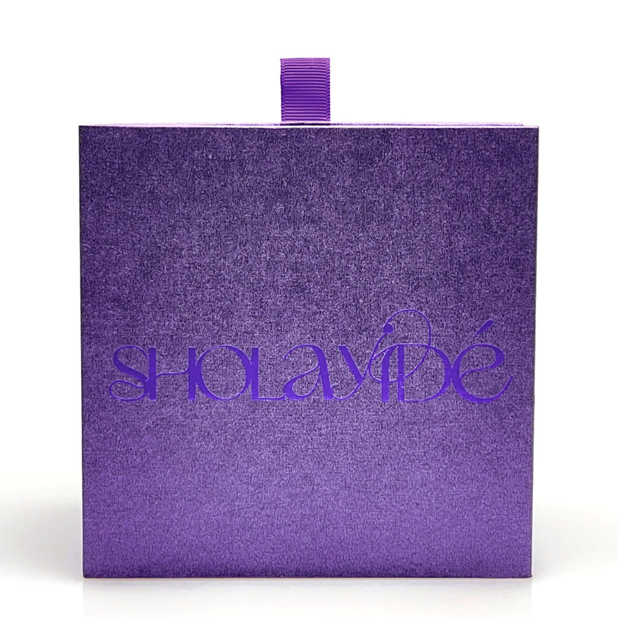 Purple textured perfume box packaging with SHOLAYIDÉ logo foil printed in purple on white background.
